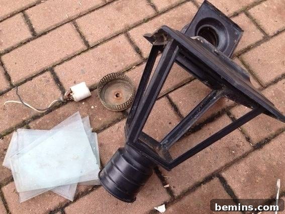 A lantern-like structure for a light, sitting disassembled on a brick surface, ready for restoration.