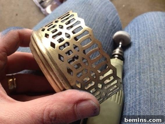 A hand holding a polished brass part above an electric polisher on a persons lap, showcasing the restoration process.