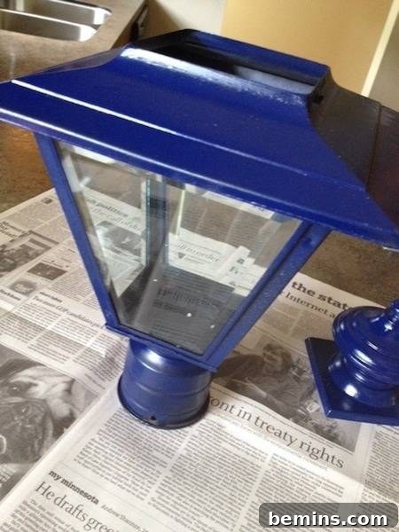 A bright blue freshly painted porch lantern sits on newspaper, showcasing its vibrant new color.