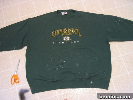 Round neck green T-shirt on the tile floor with scissors near it.