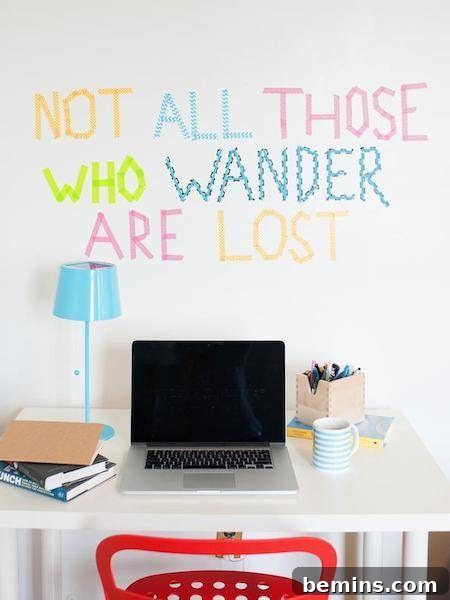 A wall has colored text on it above a laptop on a table.