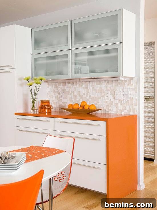 A kitchen has orange furniture and white walls.