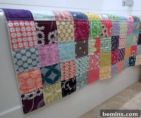 A multicolored quilt laying on the edge of a bathtub, showcasing a quilted bath mat.