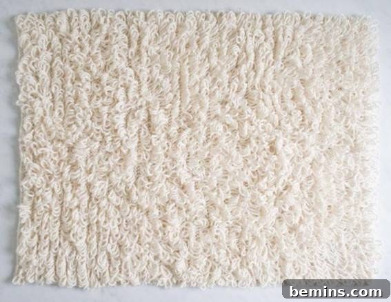 A piece of white carpet is cut out into a rectangle, showcasing a loopy knitted bath mat.
