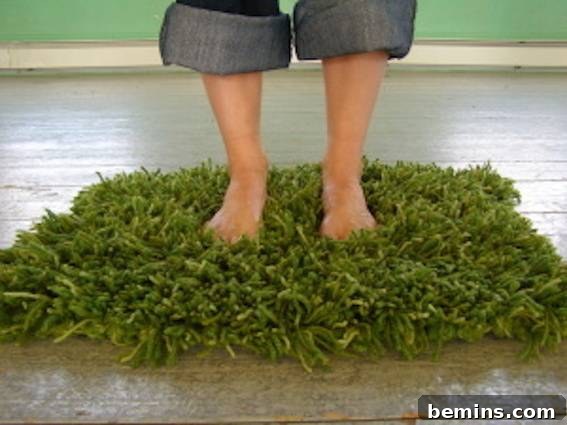 A person standing in a bathmat made of shrubbery/plants, showcasing a faux grass crochet rug.