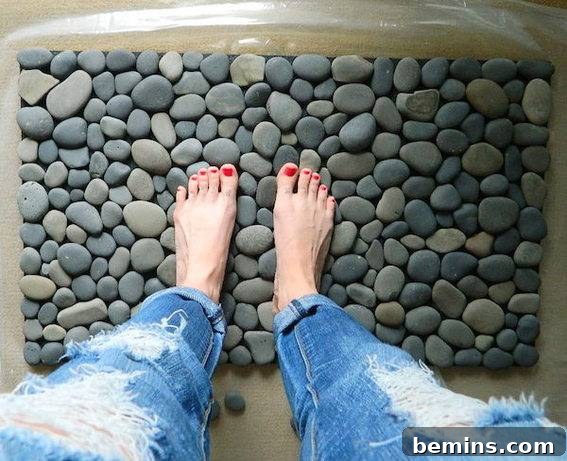 A woman's legs and feet with red nailpolish are standing on flattened round rocks, showcasing an ocean stone bath mat.