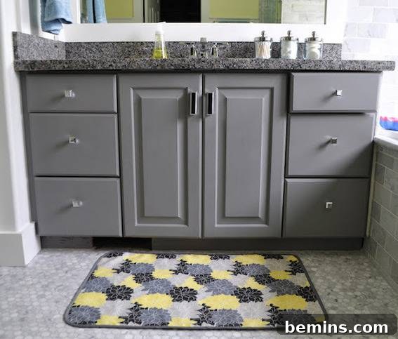 A bathroom has a rich grey cabinet, showcasing a colorful bath mat made from outdoor canvas and terrycloth.