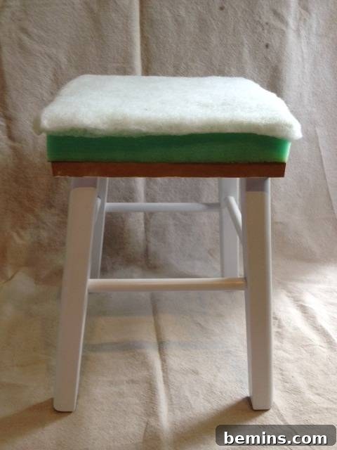 Double the Seating: A DIY Stool Split 7 White chair with a white towel, showcasing the initial upholstery layer.