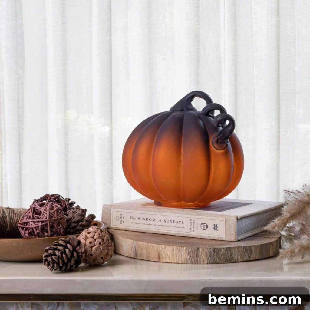 Elegant glass pumpkin centerpiece on books with pinecones and fall decor indoors.