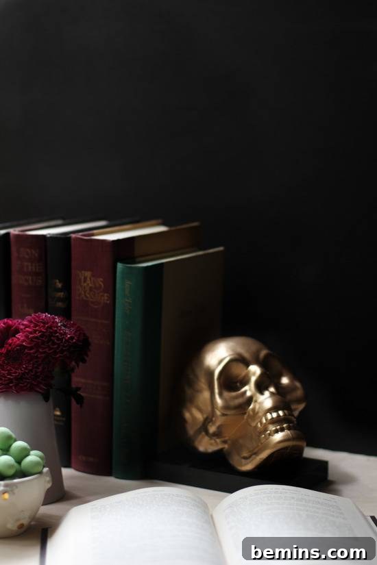 Stack of books with golden skull bookend on table.