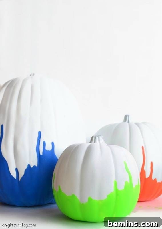 Trio of pumpkins painted in white with blue, green, and orange paint on bottoms. Vibrant neon paint dipped pumpkins DIY.