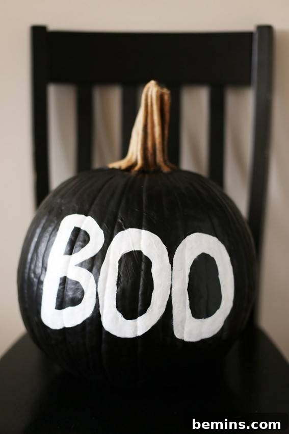 A black pumpkin has the word Book written on it in white. Classic DIY black and white painted pumpkin.