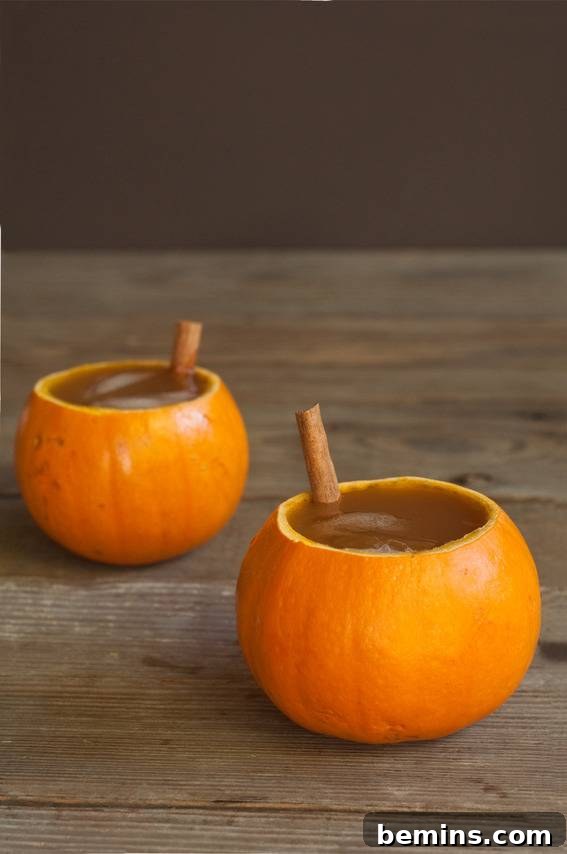 Pumpkin cups filled with a delicious beverage and garnished with cinnamon sticks.
