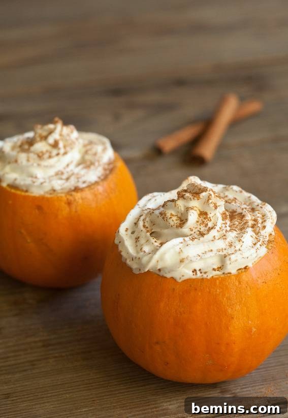 Close-up of pumpkin mugs filled with a foamy beverage and garnished with cinnamon sticks.