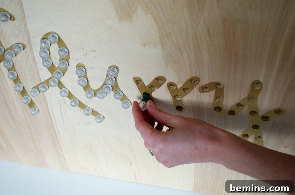 How to Design Your Own Dazzling Light-Up Sign 9 A hand carefully screwing a light bulb into one of the drilled holes, illuminating the festive sign.