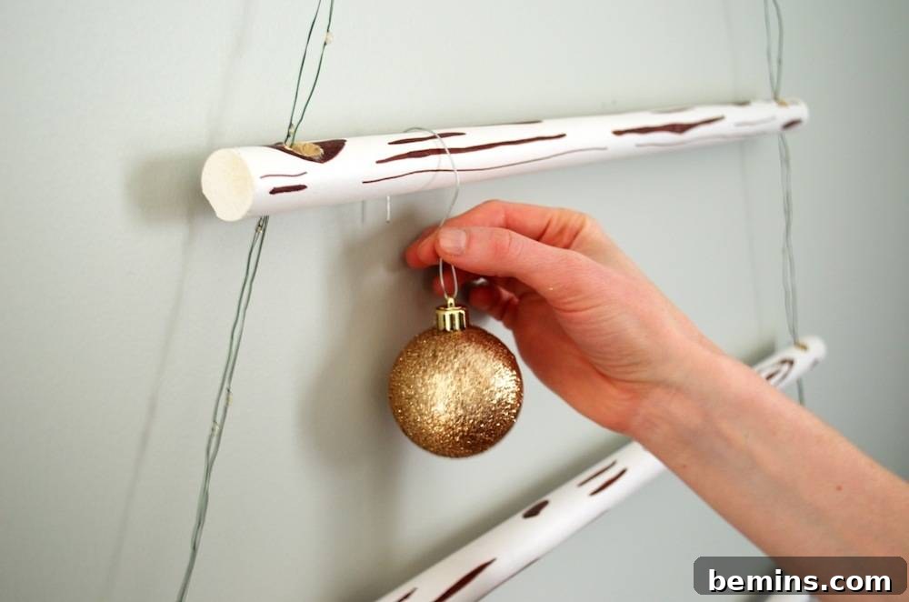 Man hanging Christmas ball to a wood hanging Christmas tree.