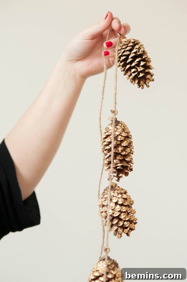 Golden Thanksgiving: 13 DIY Decor Ideas in Gold & Copper 11 A woman holding up a festive DIY golden pine cone garland.