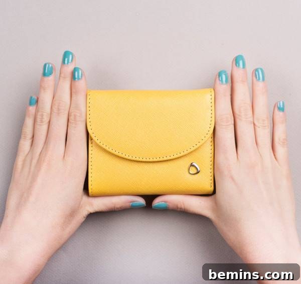 Woman with green nail polish on her nails holding a small yellow hand purse. Mini leather tri-fold wallet from Malakita.