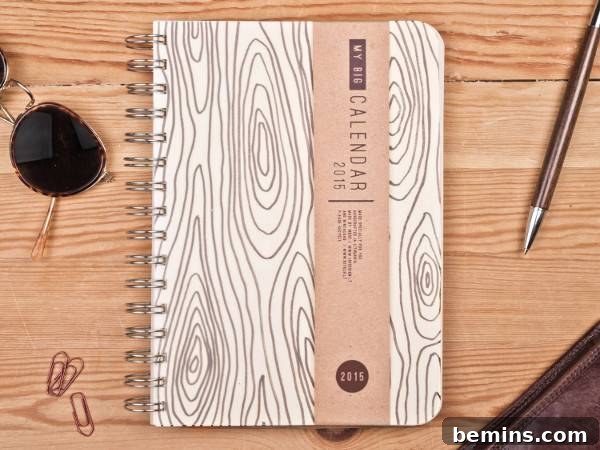 A calendar book is sitting on a wooden surface with a pen and paperclips. 2015 Weekly Planner from The Big Calendar.
