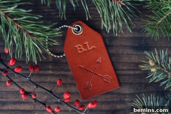A red leather tag with the initials B.L. on it with crossed arrows in surround by pine twigs and red berries on a branch. Custom Leather Luggage Tag from RSVP Handcrafted.