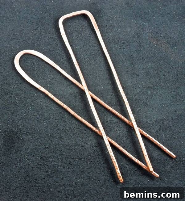 Two metal prongs sit on an off black surface showcasing the handmade copper hair forks from Dawily2. Unique hair accessory for adding a touch of elegance.