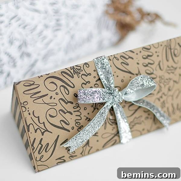 A long, thin package adorned with a silver bow and wrapped in Christmas script candy box paper.
