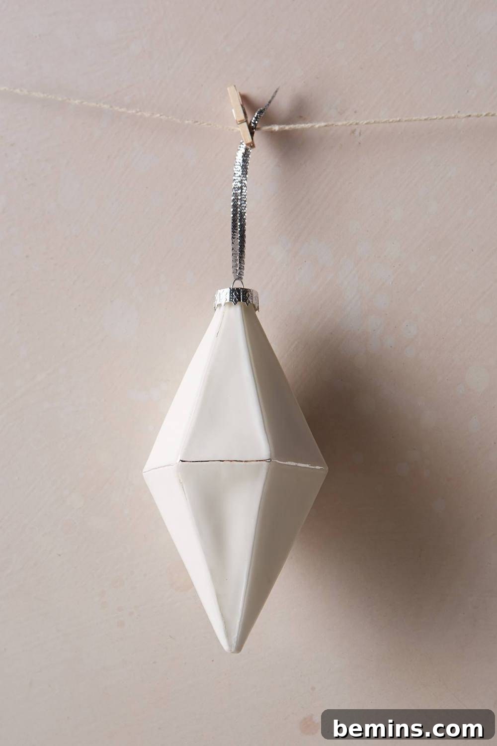 The Ultimate Ornament Roundup: 12 Must-Have Decorations for Your Tree 14 A white diamond ornament hangs on string from a hook on the wall.
