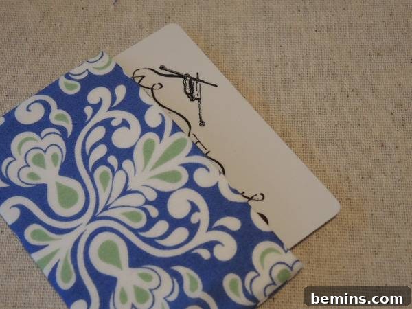 A folder with blue, green and white flower designs has a piece of paper sticking out, showing the finished bottom of the envelope with a gift card inside.