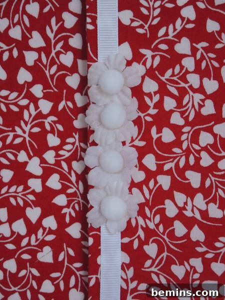 Red colored floral fabric envelop to wrap the gift, decorated with ribbon, flowers and pom poms.