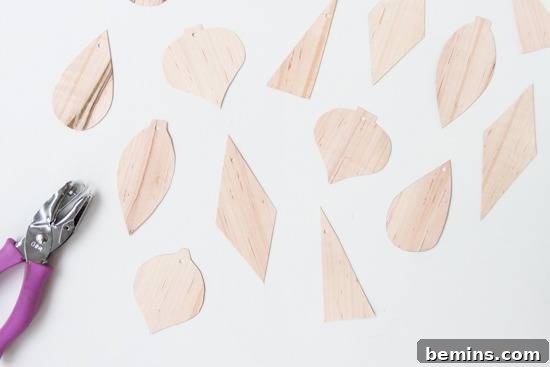 Freshly cut, unpainted veneer ornament shapes laid out on a white surface, next to a purple-handled hole punch.