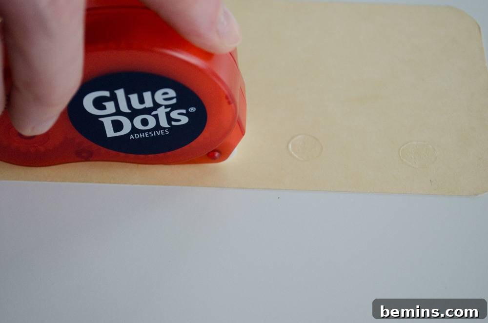 Vintage Flashcard Wall Decor Ideas 6 Hand holding a glue dots package on top of manila paper.