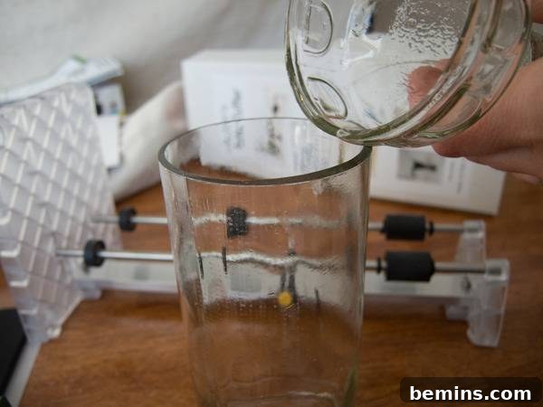 Which Bottle Cutter Reigns Supreme? A Definitive Review 45 A left hand pouring a large glass into a smaller glass on a brown table top.