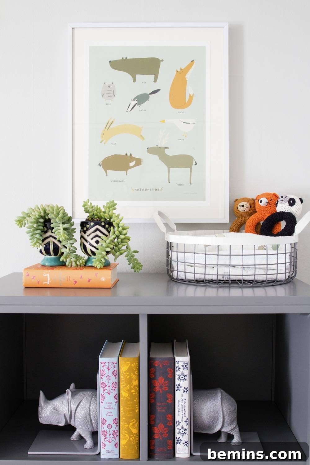A stylish gray shelf adorned with a collection of books and lush green plants, positioned beneath a captivating picture frame, creating an inviting and organized display in the nursery.