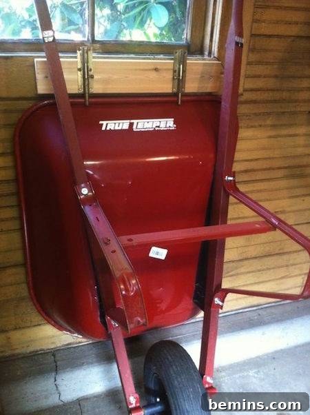 A red wheelbarrow hanging securely on the wall under a window, demonstrating a space-saving storage solution.