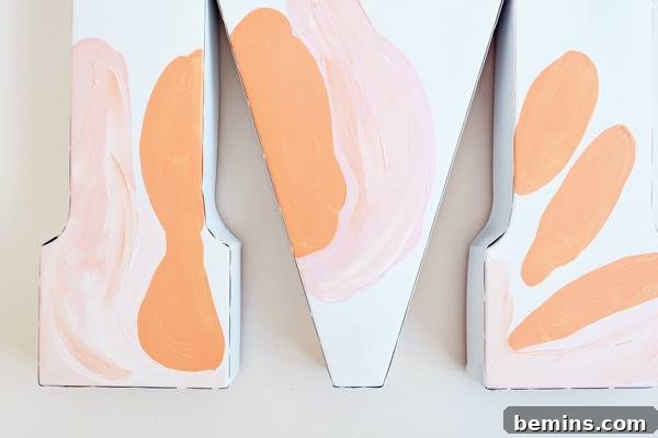 Abstract art in progress adorns a wooden letter M, displaying a blend of soft hues and emerging textures.