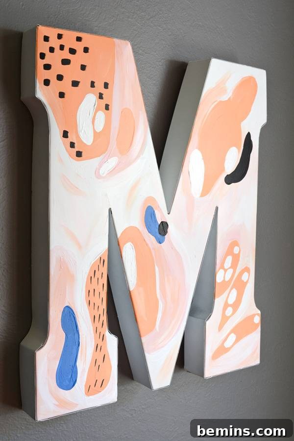 The abstract letter M, painted in delightful pink and melon hues, hangs artfully on a wall, showcasing its completed transformation.