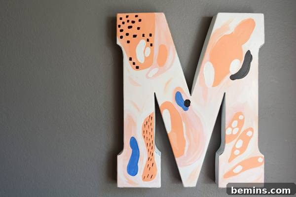 The abstract letter M, a vibrant piece of modern decor, hangs elegantly on a minimalist grey wall, blending seamlessly with contemporary aesthetics.