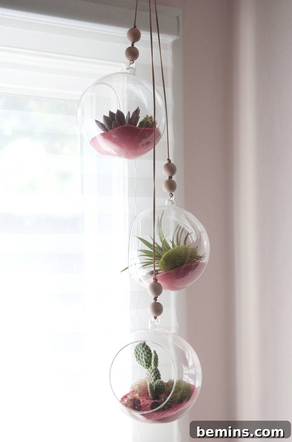 Three hanging glass plant pots near a window.