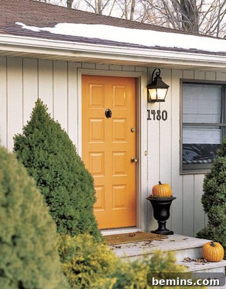 A single-story home with an orange front door and a pumpkin in a black vase on the landing, creating a warm and festive atmosphere.