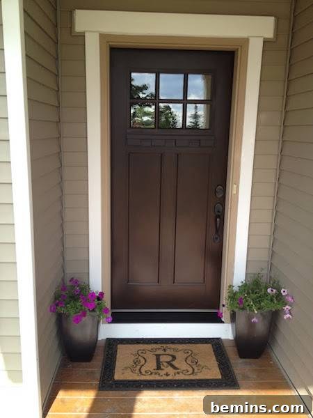 A brown Craftsman-style door flanked by plants and a welcoming doormat, creating a warm and inviting entrance.