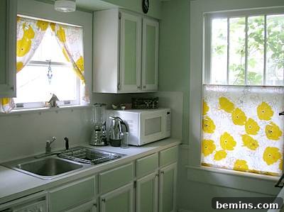 A beautiful and clean kitchen sink area with light green cabinets and white countertops.