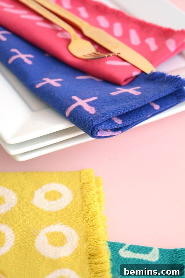 DIY Bleach Stenciled Geometric Napkins 9 A gold fork and knife sitting top of a red and pink folded napkin which sits on top of a blue and ping folded napkin which is sitting on three white plates behind a yellow piece of cloth with white circles on it.