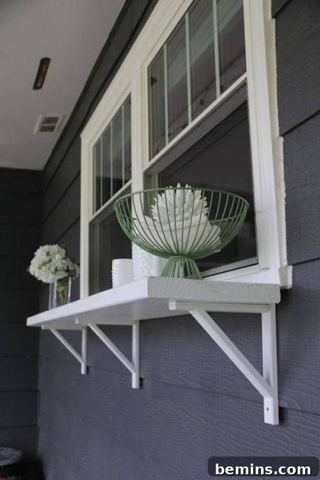 Flowers are shown on the outside of a window of a grey house.