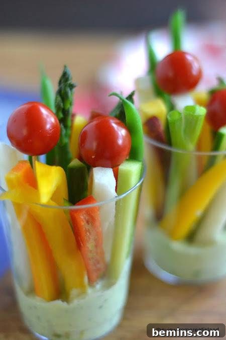 A variety of veggies are sitting in clear cups with ranch at the bottom.