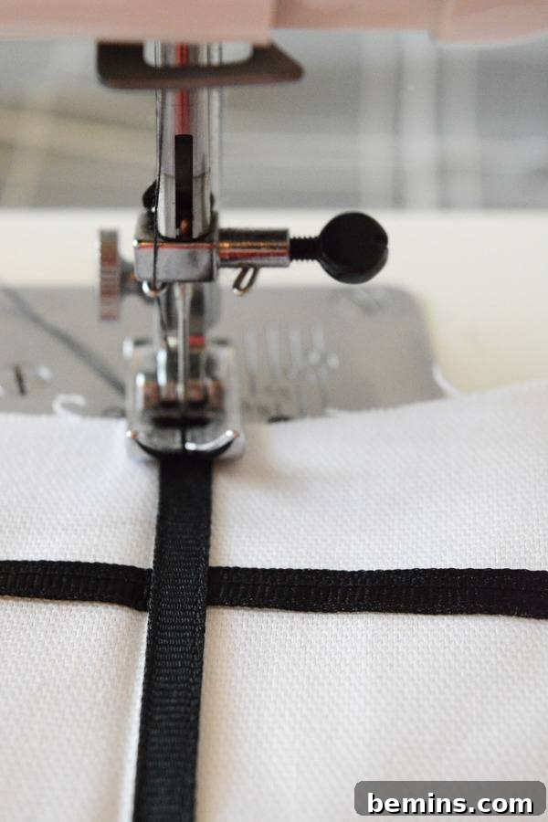 Stylish Geometric Pillows Easy DIY Guide 11 A sewing machine in action, meticulously stitching a black ribbon onto white fabric to create precise horizontal grid lines.