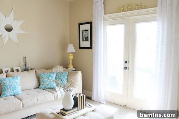 A white sofa with blue pillows sits in the corner of a room near a double door made of glass.
