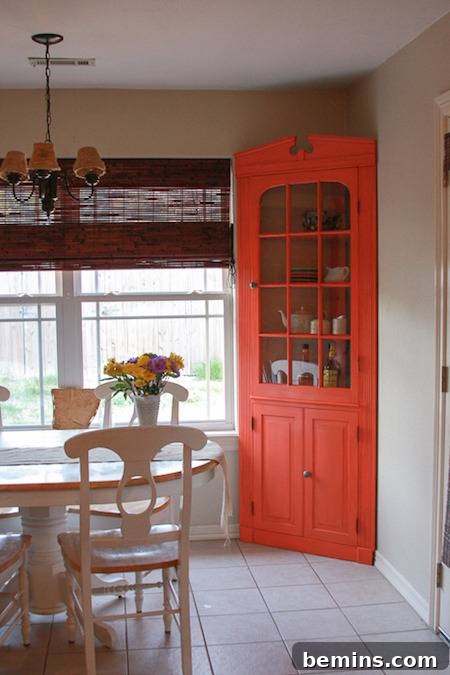 A white table and chairs in a dining room, complemented by an eye-catching orange sideboard in the corner.