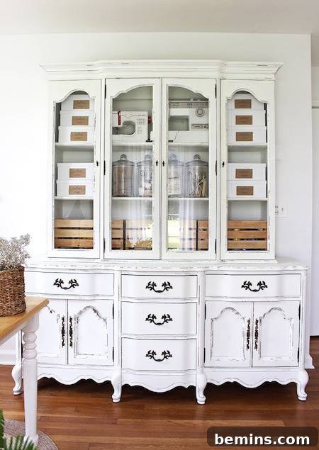A white hutch china cabinet placed against a wall on top of a dark wood floor, creating a sophisticated contrast.