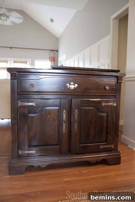 A dark brown side table with brass hinges resting on a wood floor in a white room.