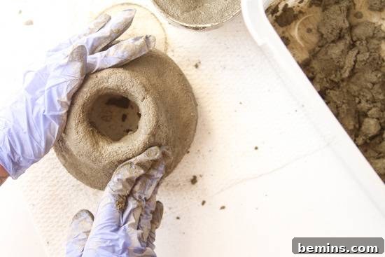 A person wearing gloves is molding a vase out of shapable concrete.